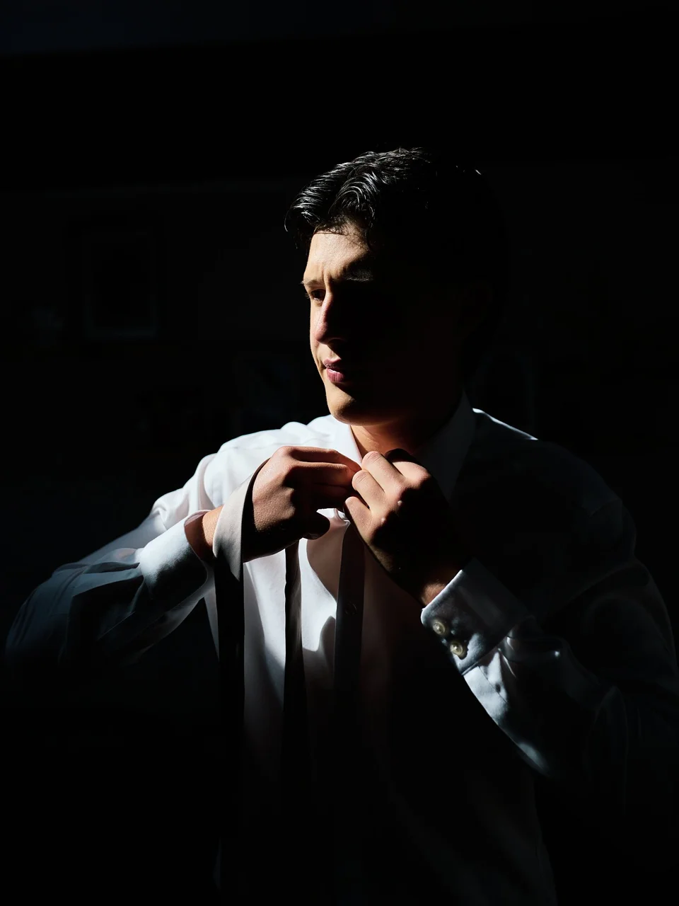 The groom adjusting his tie by a window